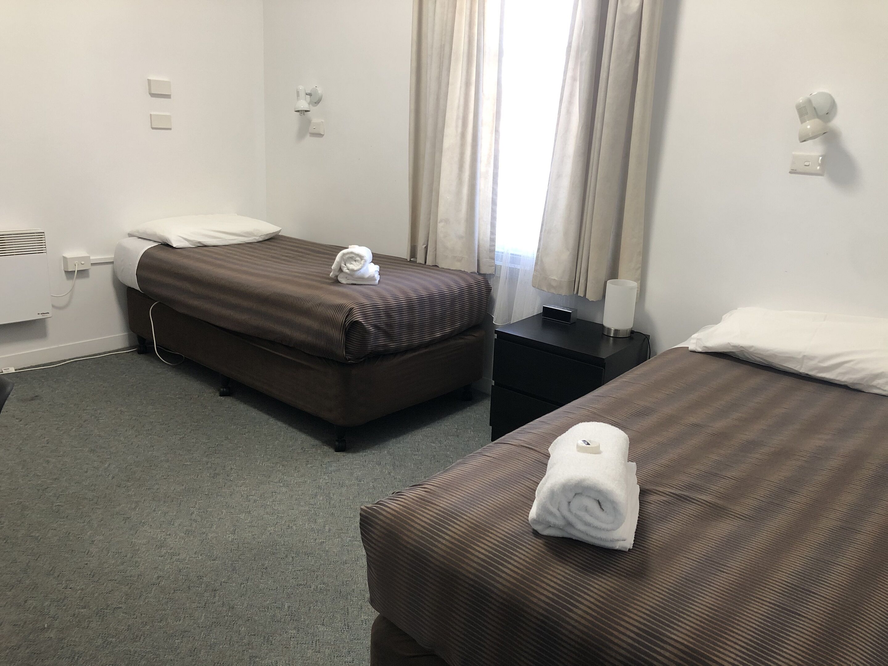 Una habitación de hotel con dos camas, una mesita de noche, una lámpara y una ventana con cortinas.
