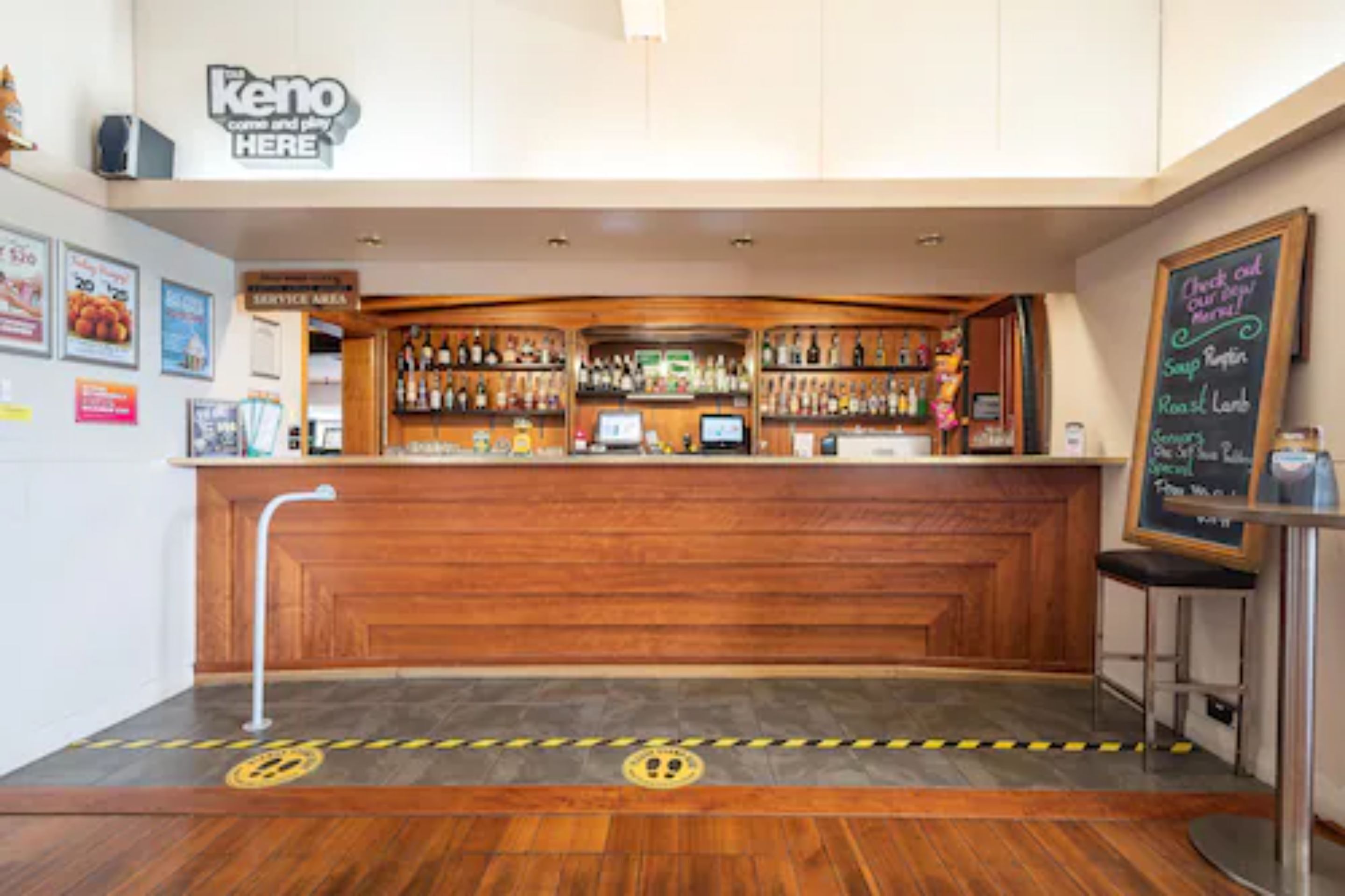 A bar area with a wooden counter, shelves with bottles, a service area sign, and a chalkboard menu.