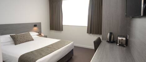 A hotel room with a bed, a desk with a kettle and toaster, and curtains on the window.