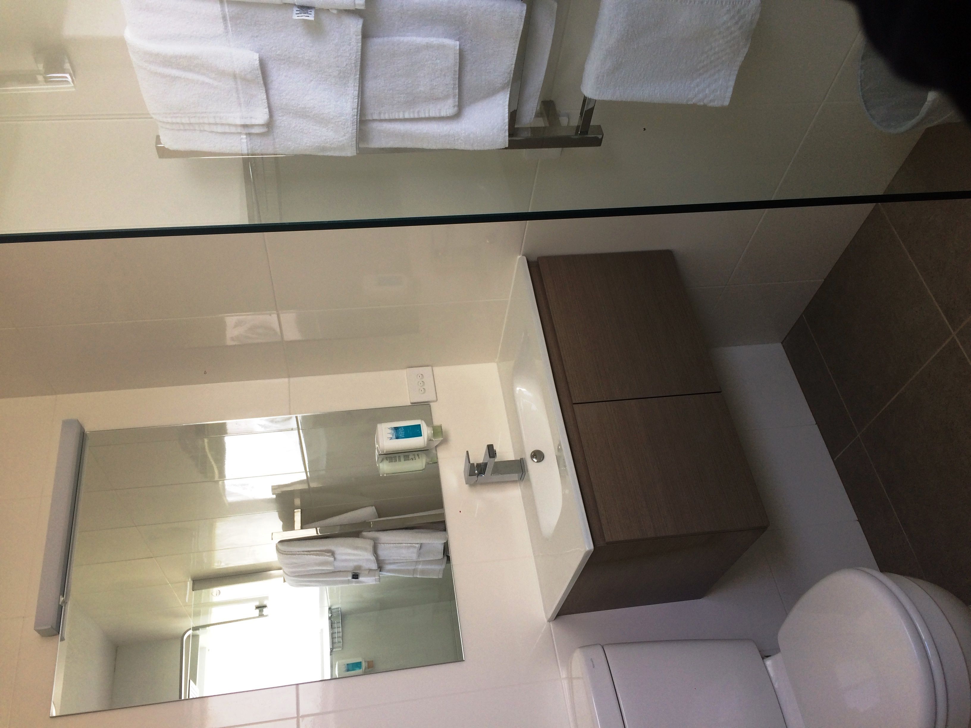 A bathroom with a glass shower enclosure, a white toilet, a sink with a mirror, and a wooden cabinet.