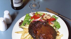 Un plato con una hamburguesa, papas fritas, una ensalada, una botella de vino y saleros y pimenteros sobre una mesa.