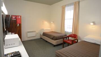 Une chambre d’hôtel avec deux lits simples, un bureau avec un ordinateur, une chaise et une fenêtre avec des rideaux.
