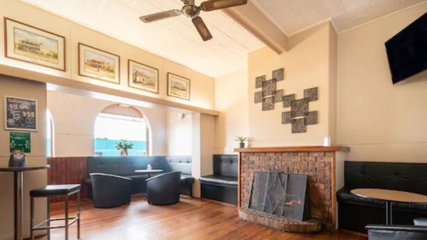 A spacious lobby with a wooden floor, a fireplace, seating areas, and framed pictures on the walls. - The Bridge (Smithton)