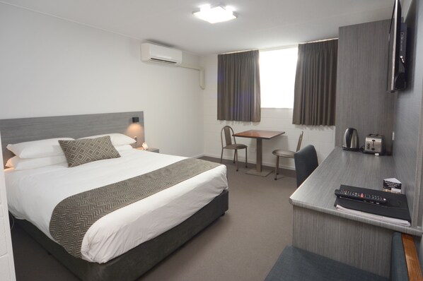 Una habitación de hotel con una cama, un escritorio, una silla, un televisor y una cafetera.