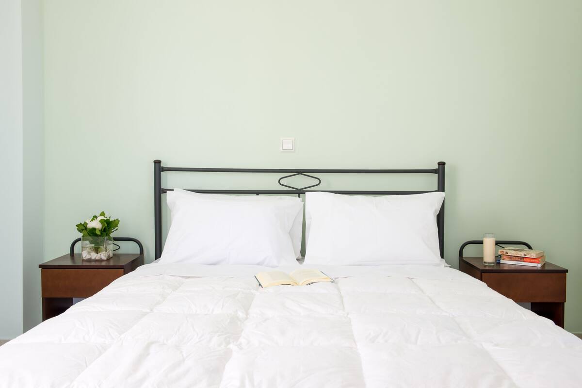 A neatly made bed with white bedding, a book, and a glass of milk on a bedside table.