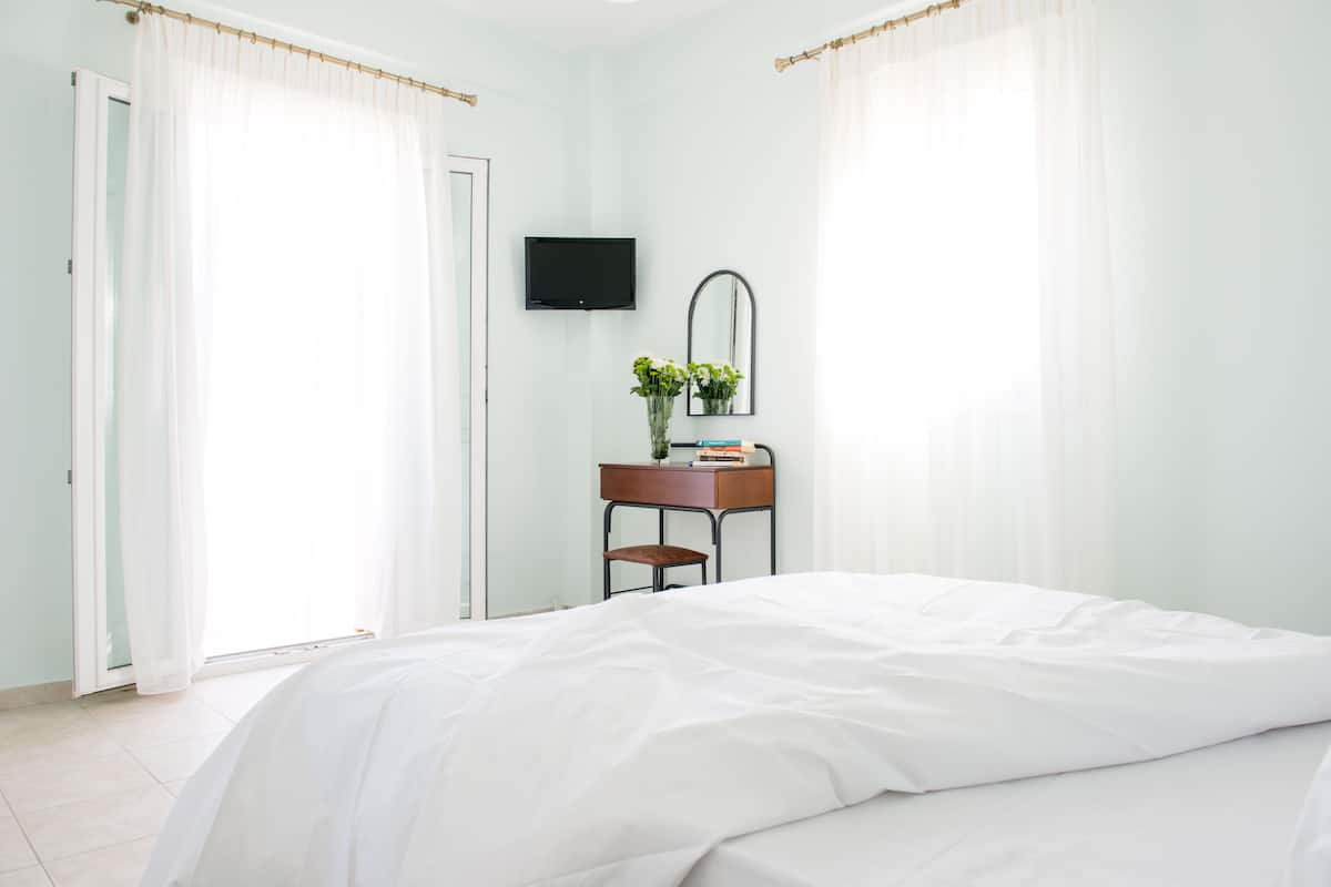 A bedroom with a bed, a desk with a chair, a flat-screen TV, and a mirror.
