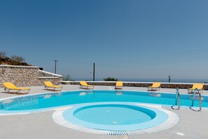 Una piscina con pared de piedra y sillas de descanso amarillas.