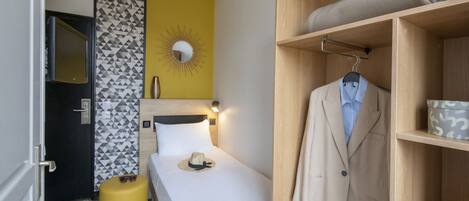 Quarto de hotel com cama, guarda-roupa, um banquinho amarelo e espelho com desenho de sol.