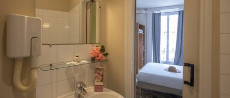 A bathroom with a sink, mirror, and a glass shelf with toiletries.