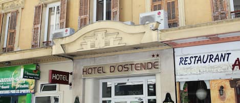 Un hôtel à la façade classique, doté de nombreuses fenêtres avec volets et d’une enseigne indiquant qu’il s’agit d’un hôtel.