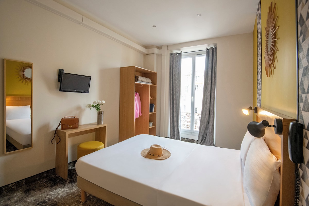A hotel room with a bed, a desk, a television, a wardrobe, and a window with curtains.