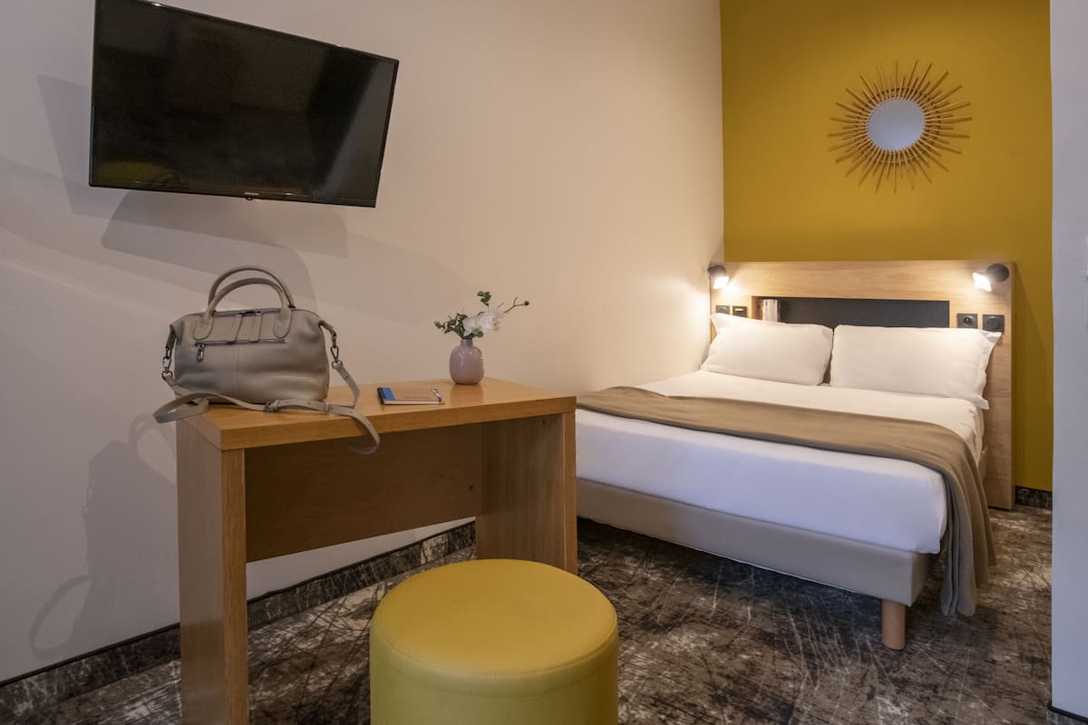 A hotel room with a bed, a desk, a chair, a TV, and a wall-mounted sun decoration.