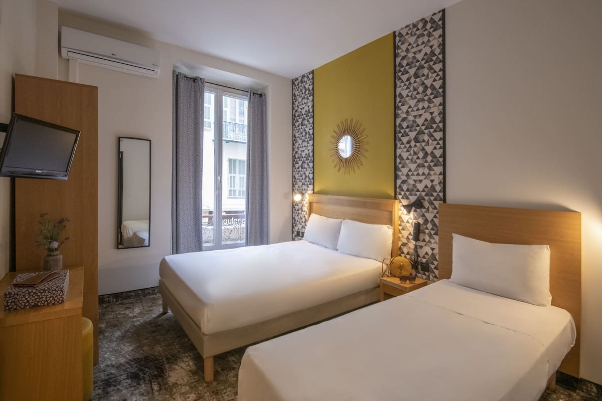 A hotel room with two beds, a TV, a mirror, and a window with curtains.