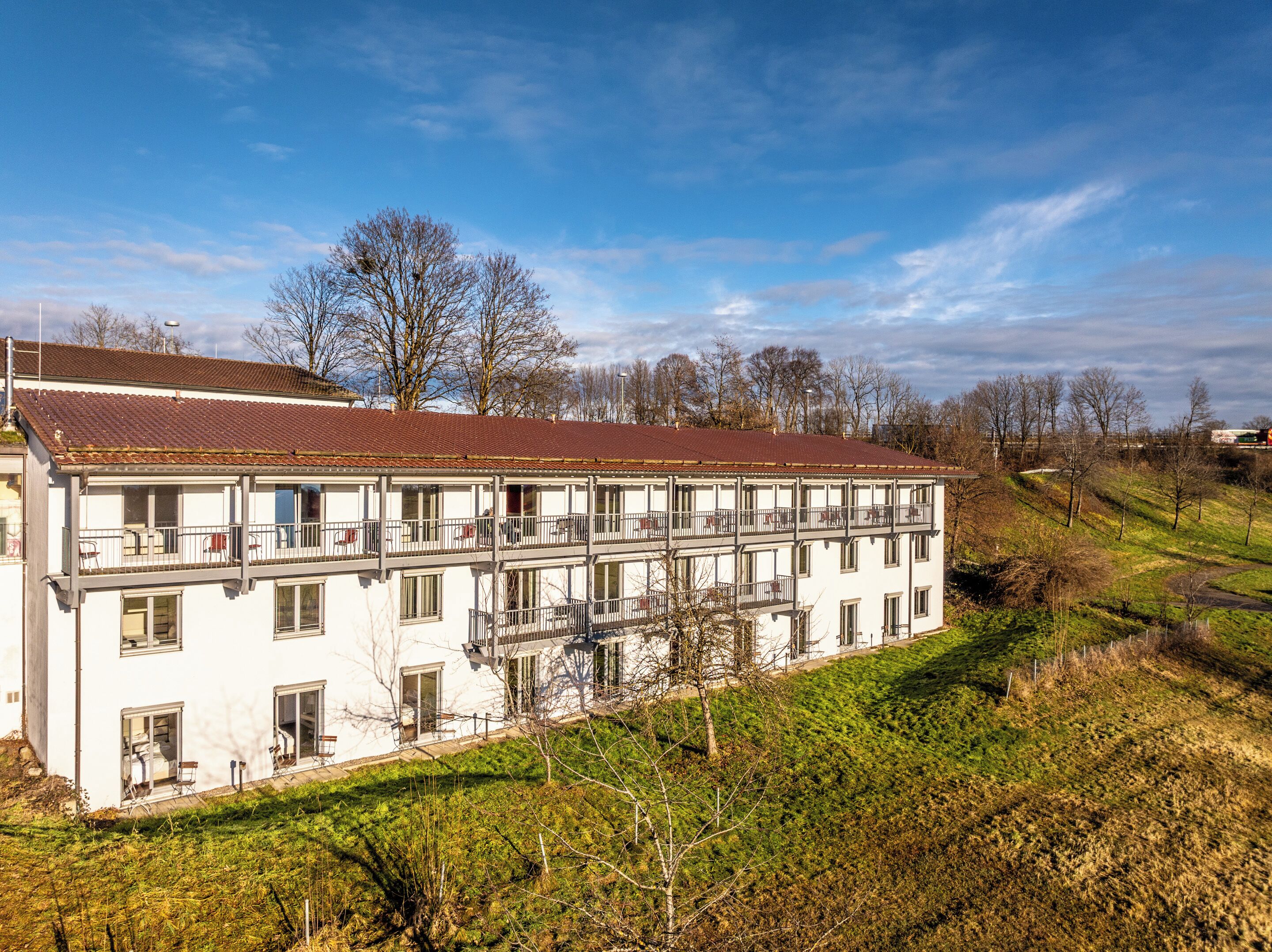 A two-story building with balconies, a red-tiled roof, and a garden area in front.
