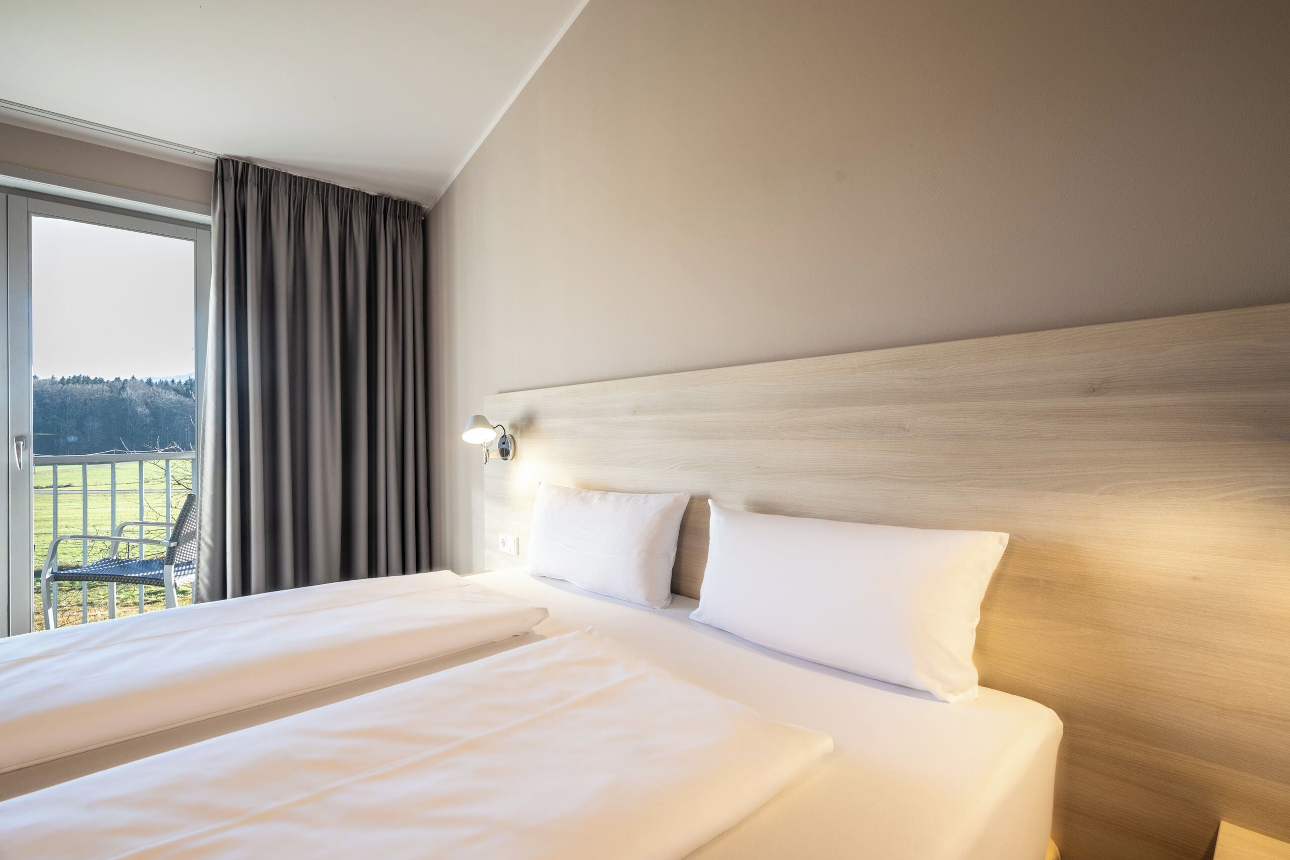 Una habitación de hotel con una cama grande, un cabecero de madera y una ventana con cortinas.