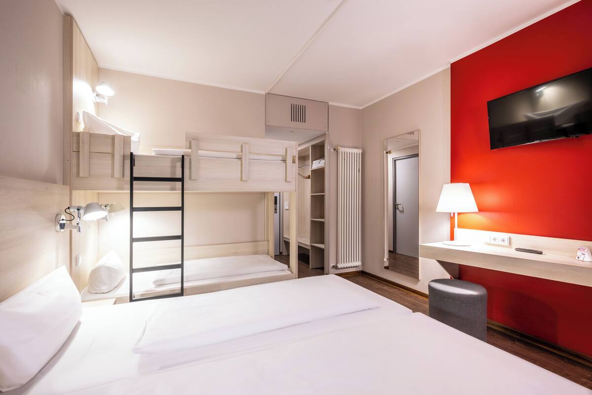A hotel room with a bunk bed, a desk with a lamp, a TV, and a wardrobe.