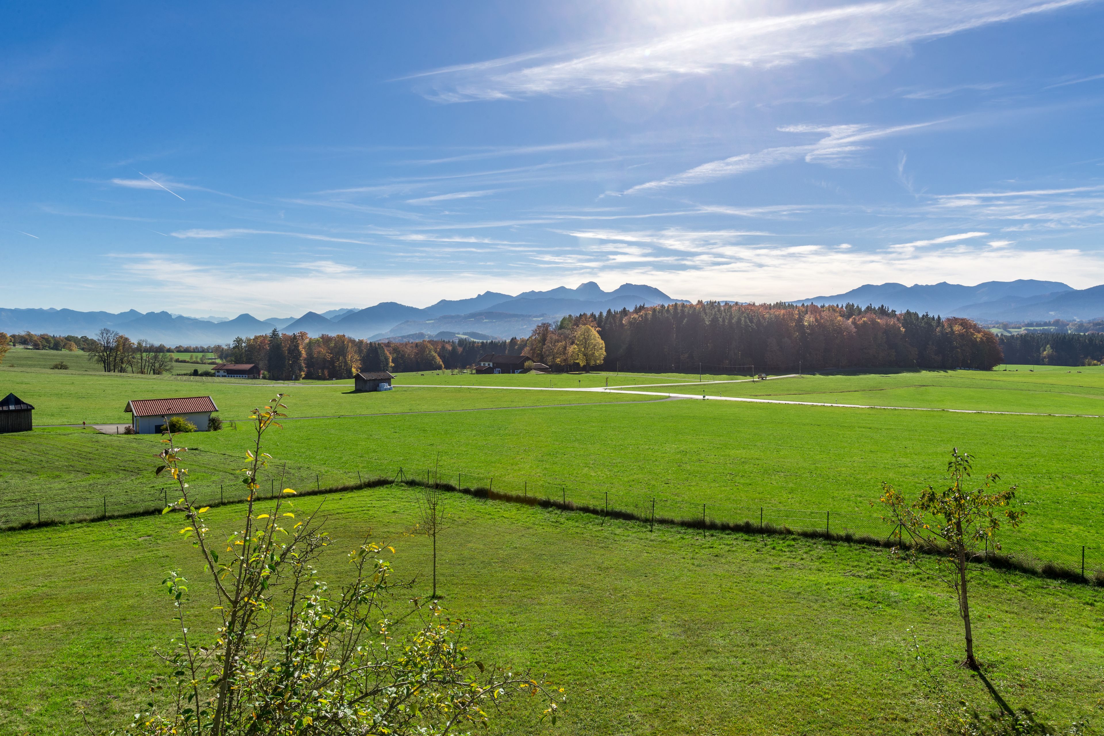 A rural landscape with a large green field, a small building, and mountains in the background.