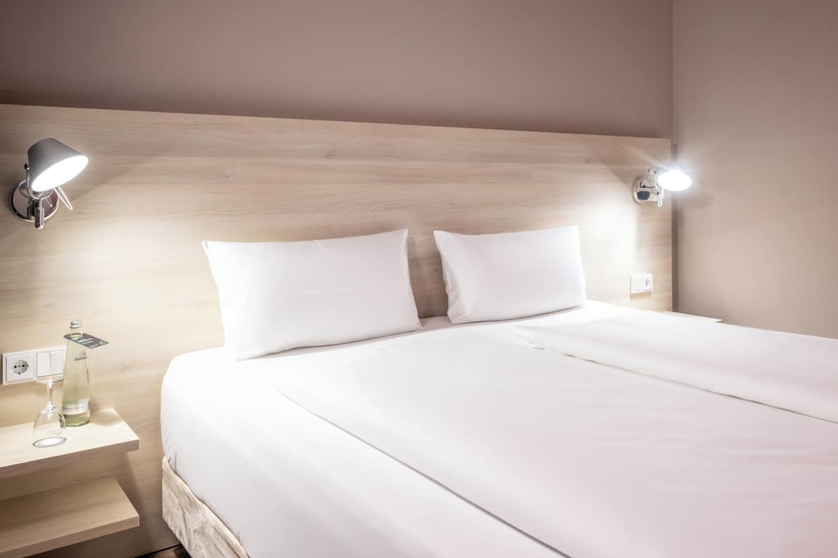A neatly made bed with white linens, two bedside lamps, and a bottle of water on a wooden nightstand.