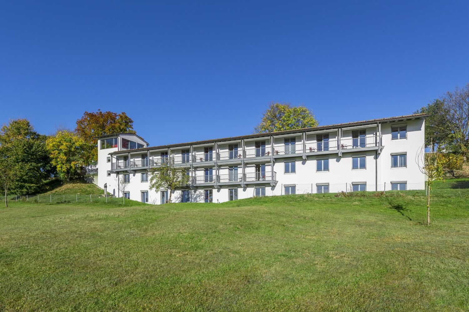 Un edificio a più piani con balconi, immerso nel verde tra prati e alberi.