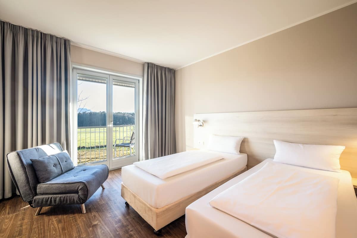 A hotel room with two beds, a sofa, and a large window with curtains.