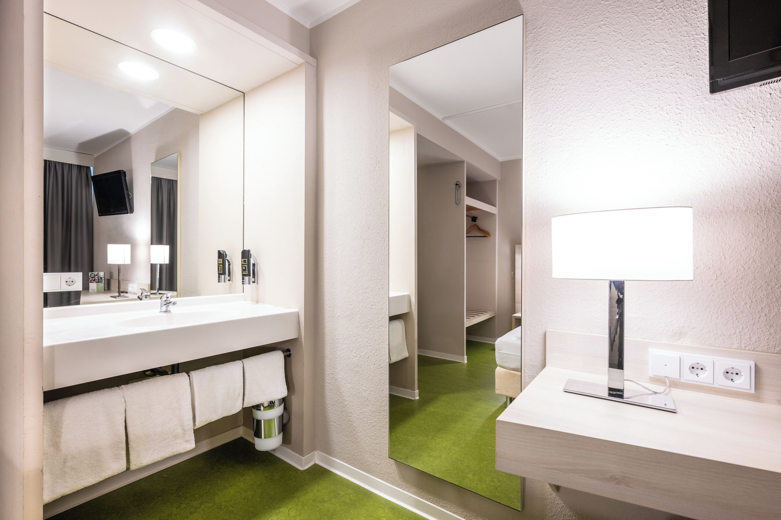 Une salle de bain moderne avec un grand miroir, deux lavabos, un porte-serviettes et un sol vert.