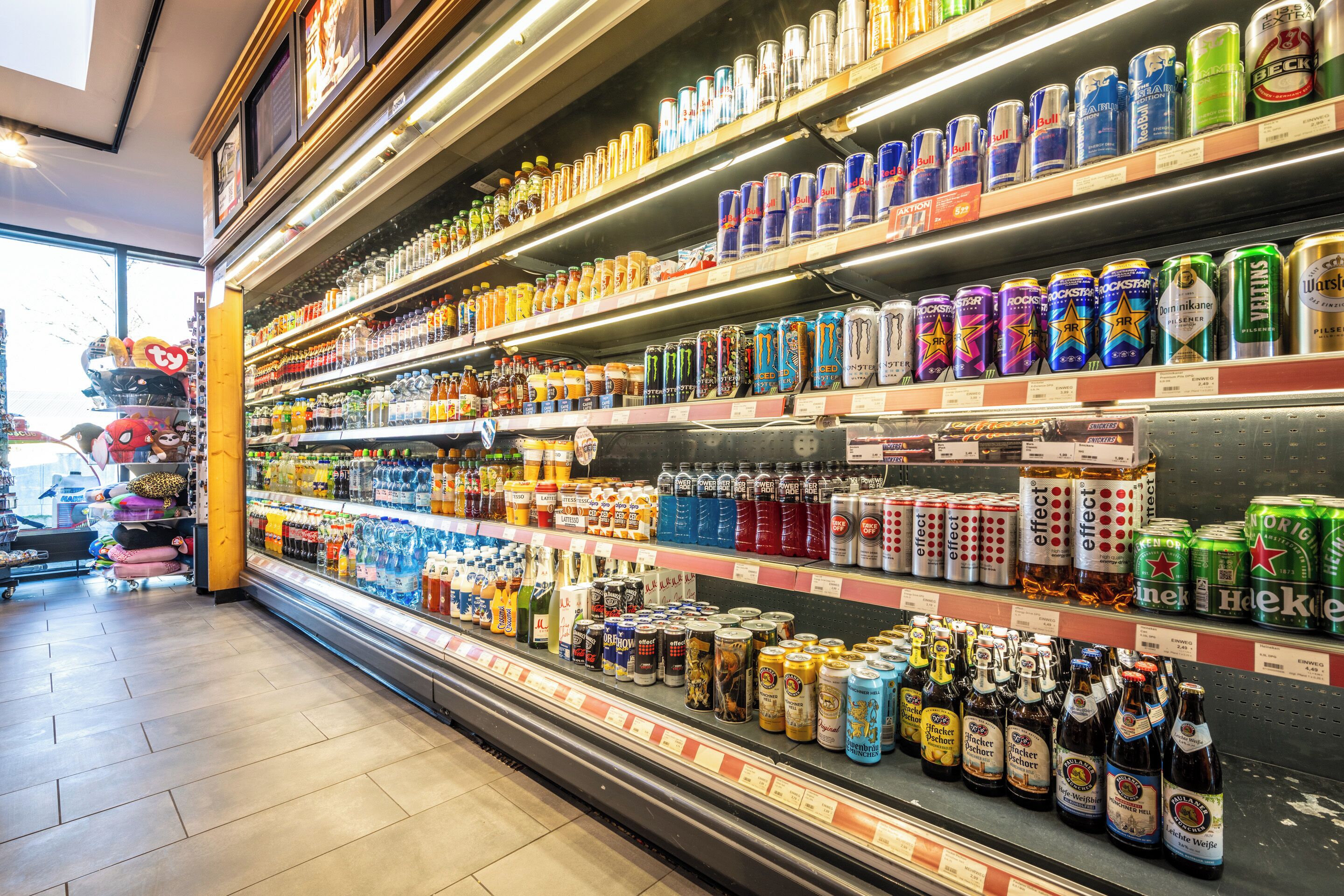 Una sección refrigerada en una tienda con diversas bebidas, incluyendo latas y botellas, sobre estantes.