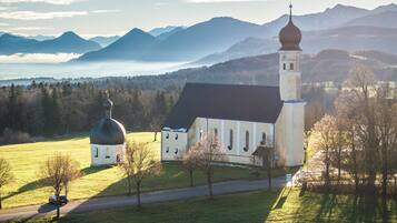 Uma igreja com uma cúpula imponente e um campanário, rodeada por uma paisagem verde e montanhas ao fundo.