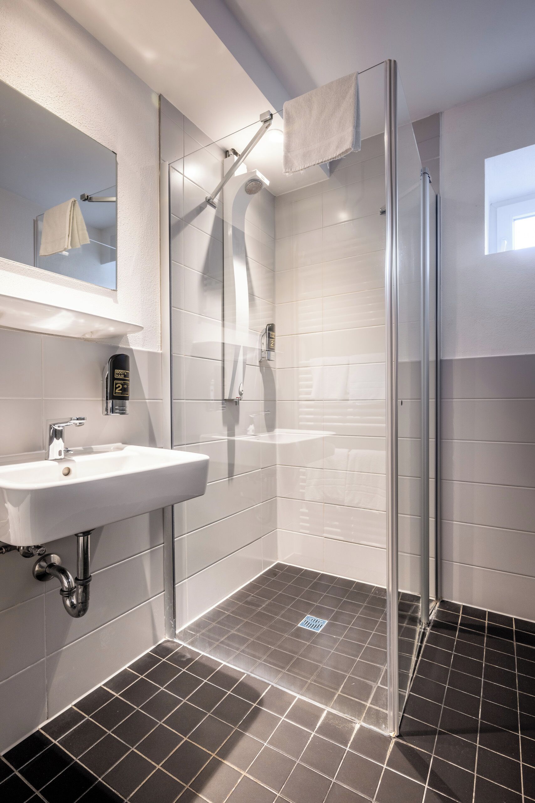 Un bany modern amb un espai de dutxa de vidre, un lavabo blanc i un mirall a la part superior.