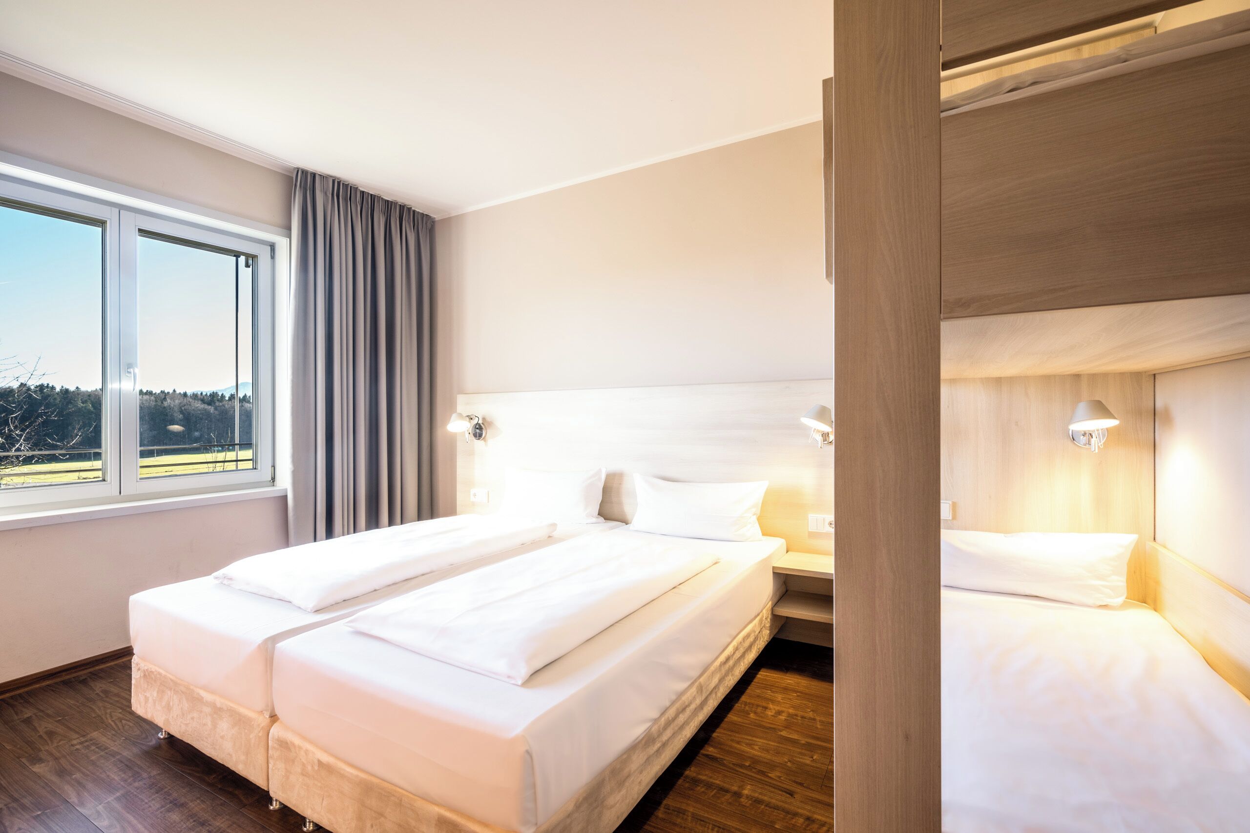 Una habitación de hotel con una cama grande, una mesita de noche, una ventana con cortinas y vistas al exterior.
