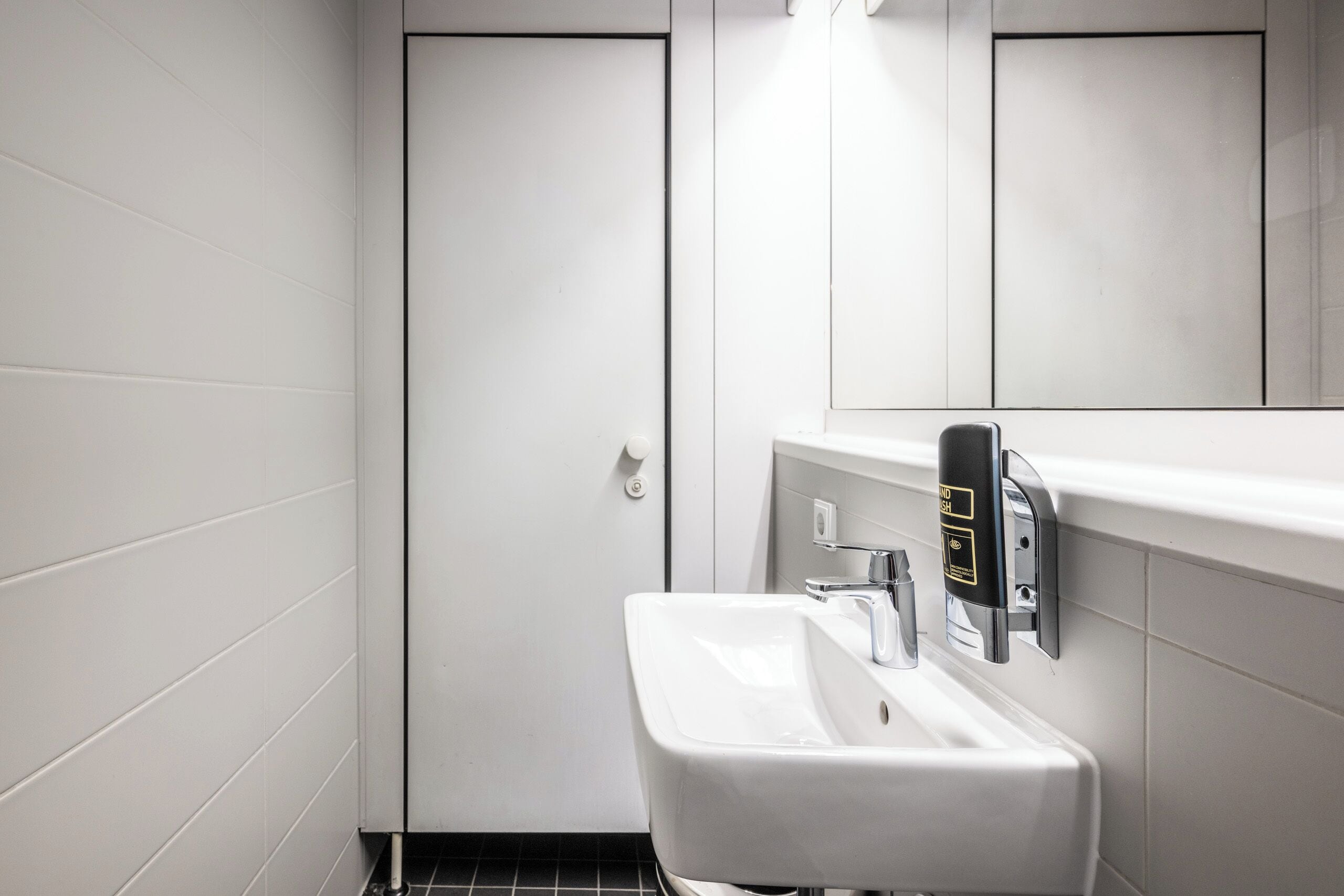 Un baño moderno con un lavamanos blanco, un espejo y un dispensador de jabón.