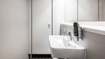 Un baño moderno con un lavamanos blanco, un espejo y un dispensador de jabón.