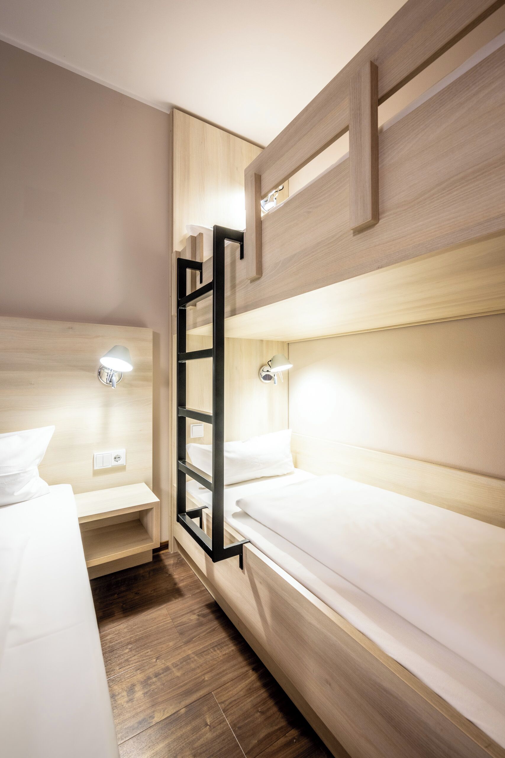 A modern hotel room with bunk beds, wooden paneling, and built-in lighting.