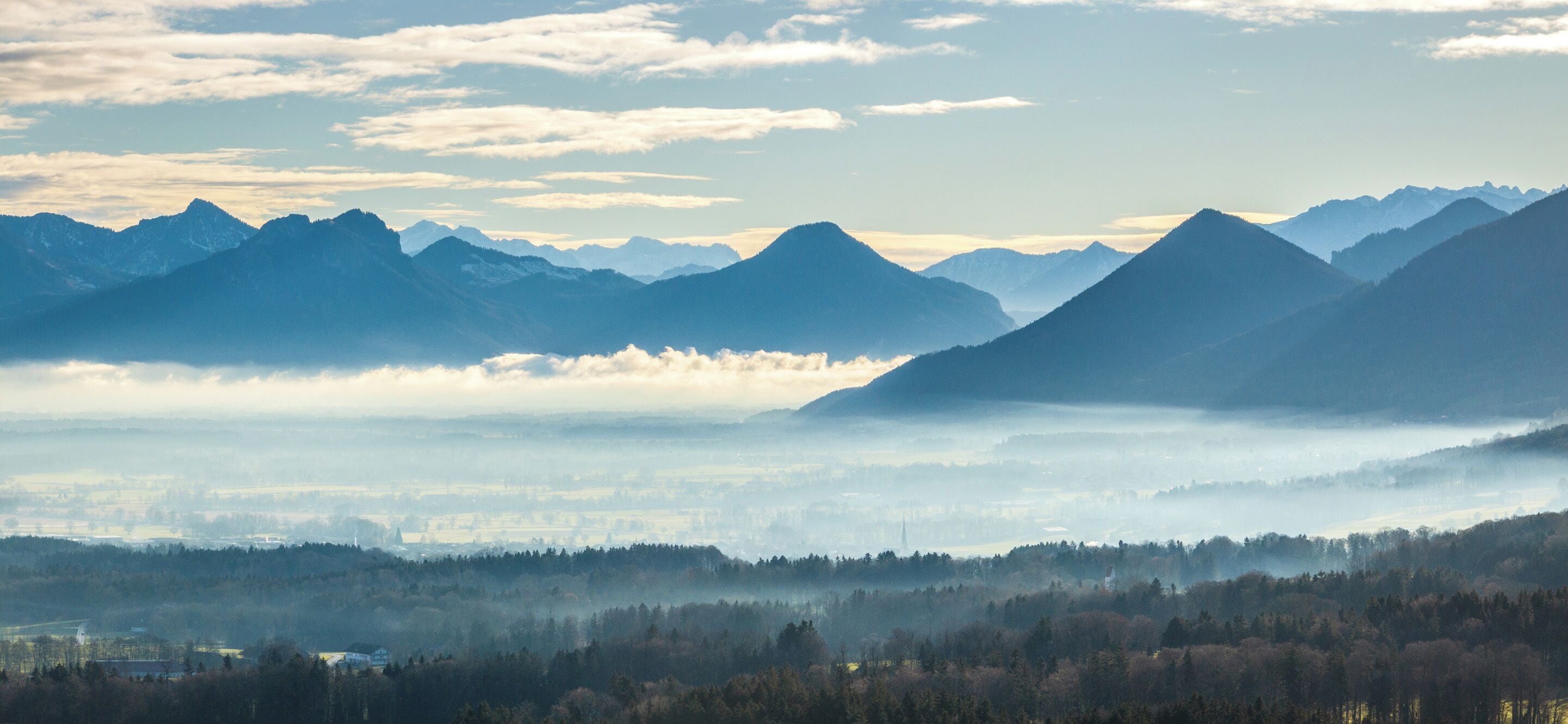 Berglandschap met een vallei en een door mist gehuld stadje eronder.