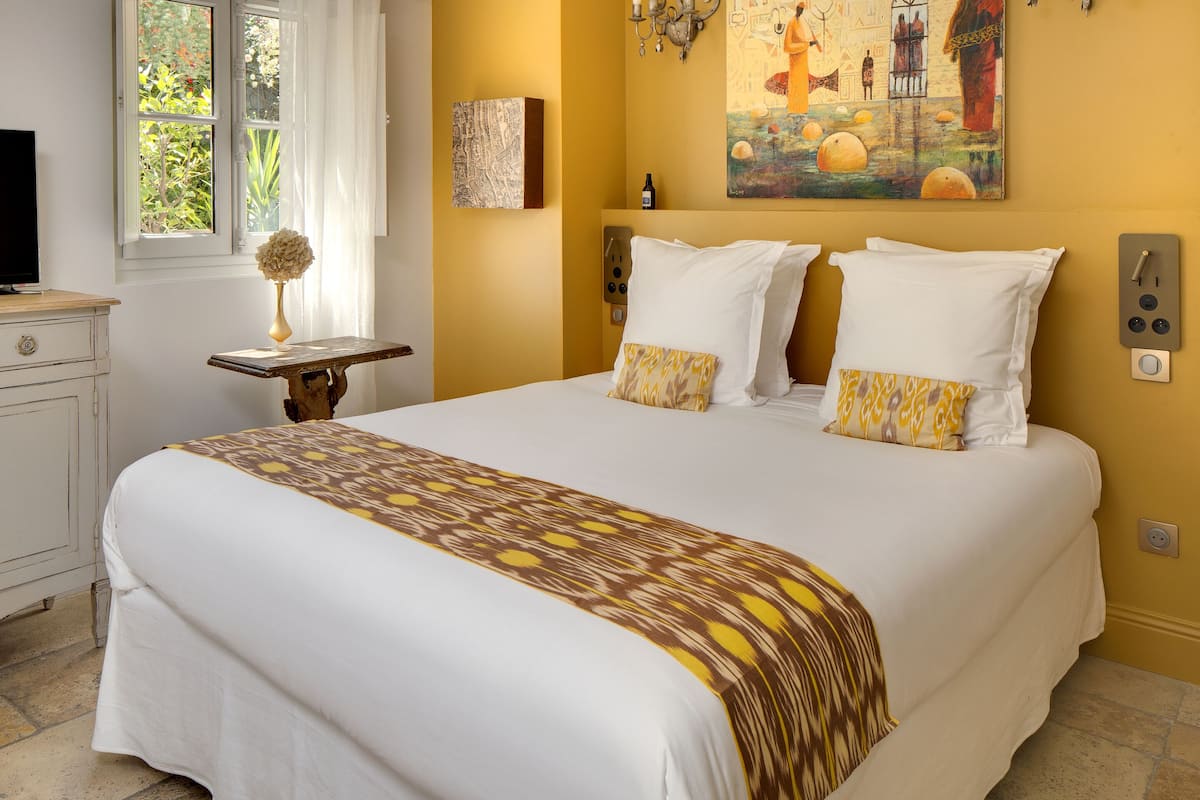 A neatly made bed with white linens and patterned pillows, a bedside table with a lamp, and a painting on the wall.