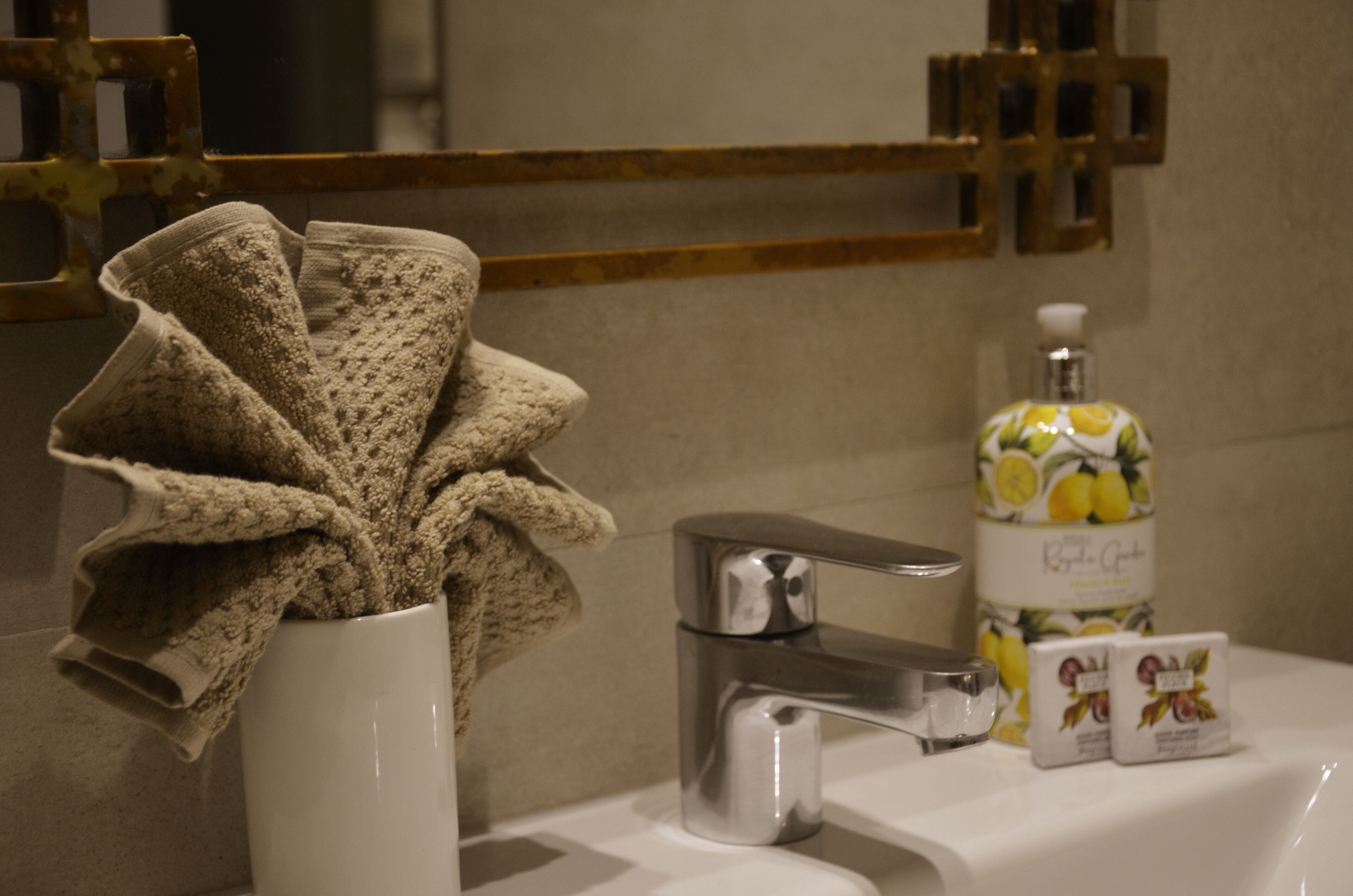 Une salle de bain avec un lavabo blanc, un robinet chromé, une serviette et un flacon de savon.