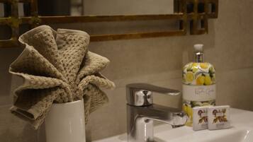 Une salle de bain avec un lavabo blanc, un robinet chromé, une serviette et un flacon de savon.