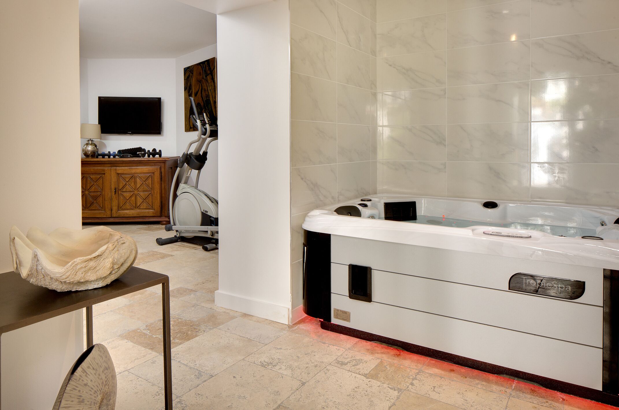 A modern bathroom with a large bathtub, a wooden cabinet, and exercise equipment.