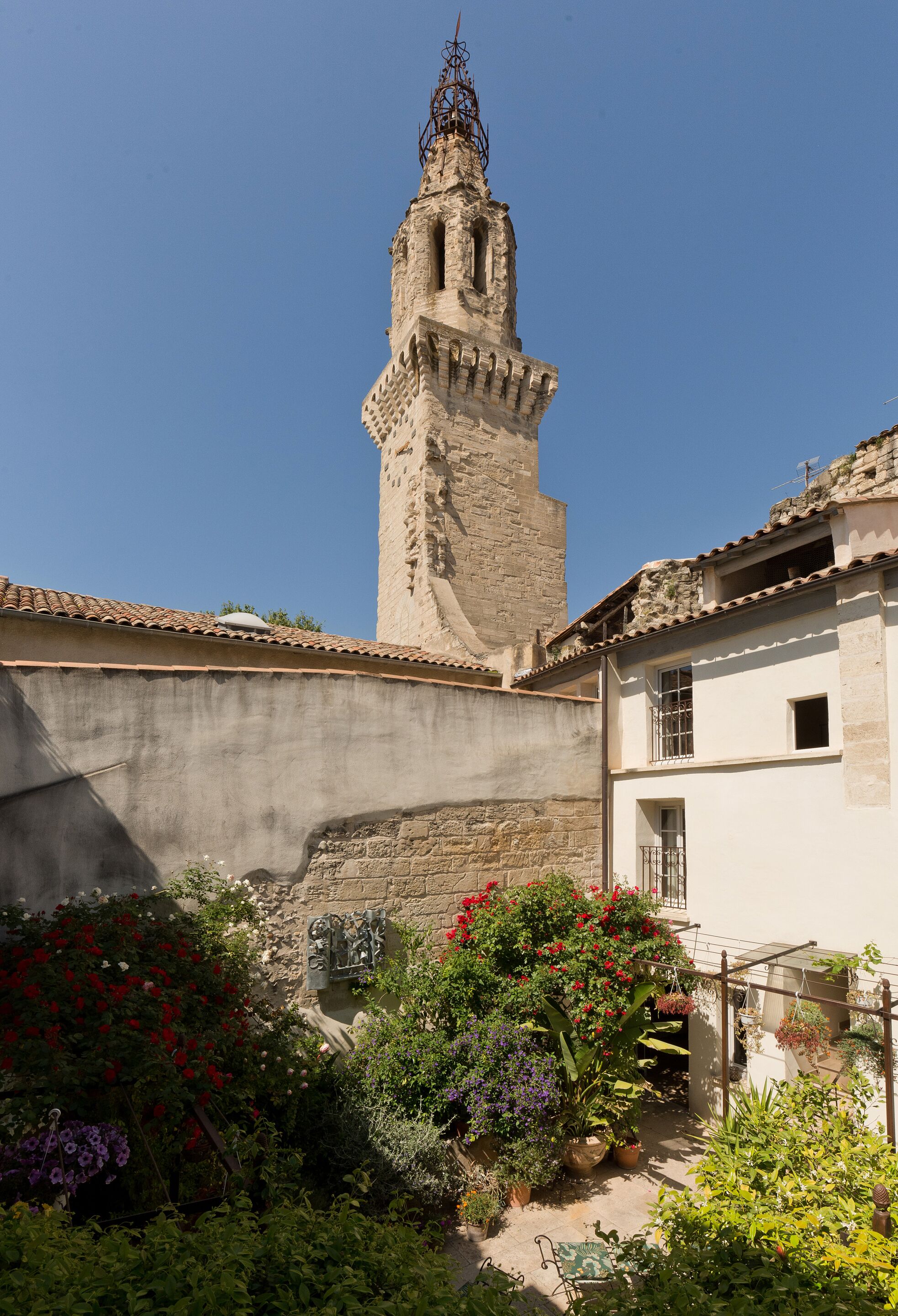 A courtyard with a tower, potted plants, and a building with a tiled roof.