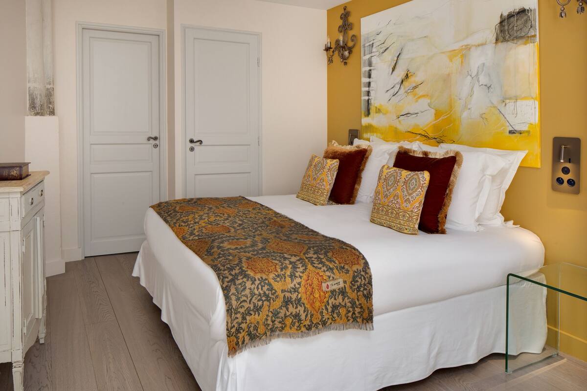 A bedroom with a large bed, a bedside table, and a wall-mounted artwork.