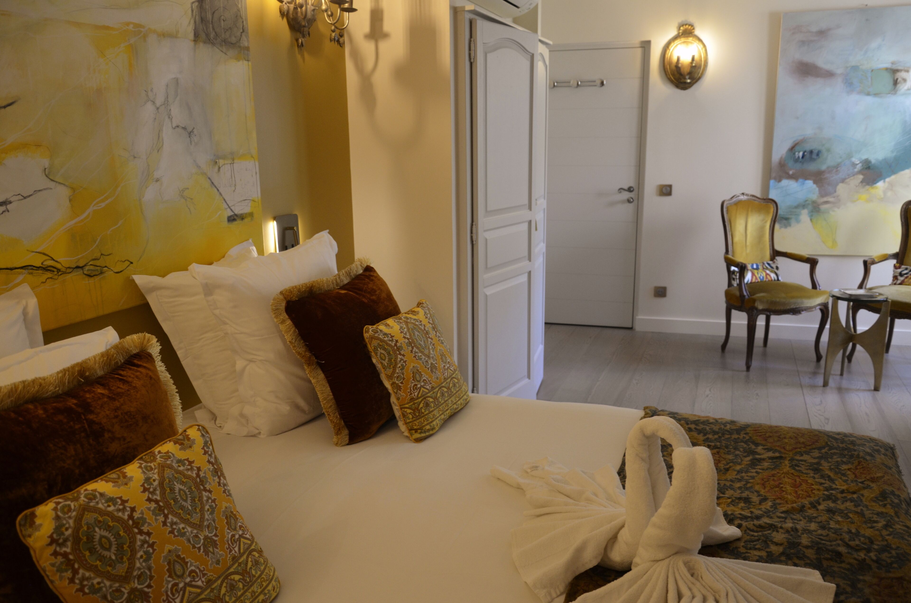 A hotel room with a bed, pillows, a chair, and a painting on the wall.
