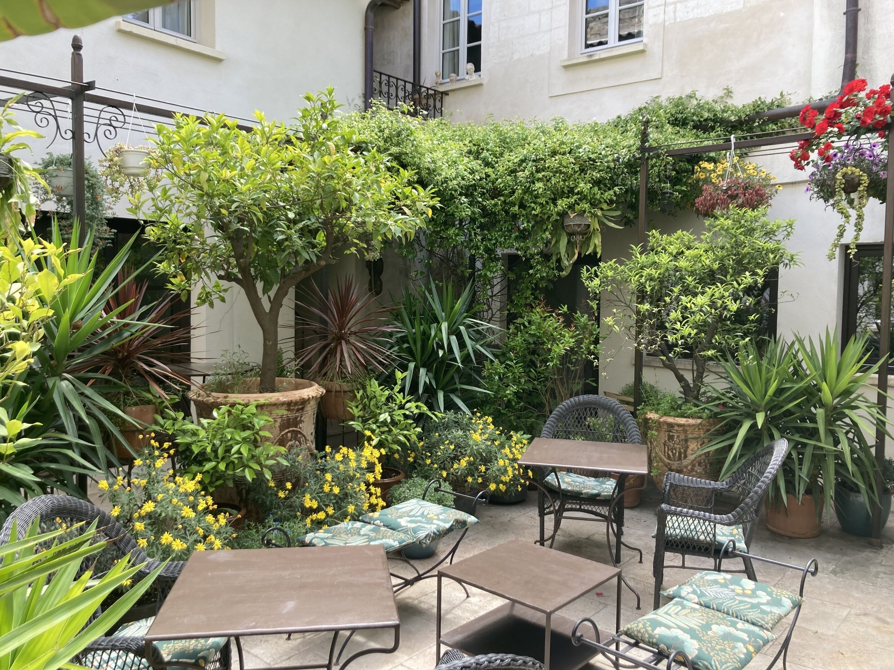 Un patio al aire libre con mobiliario de mimbre, plantas en macetas y cestas de flores colgantes.