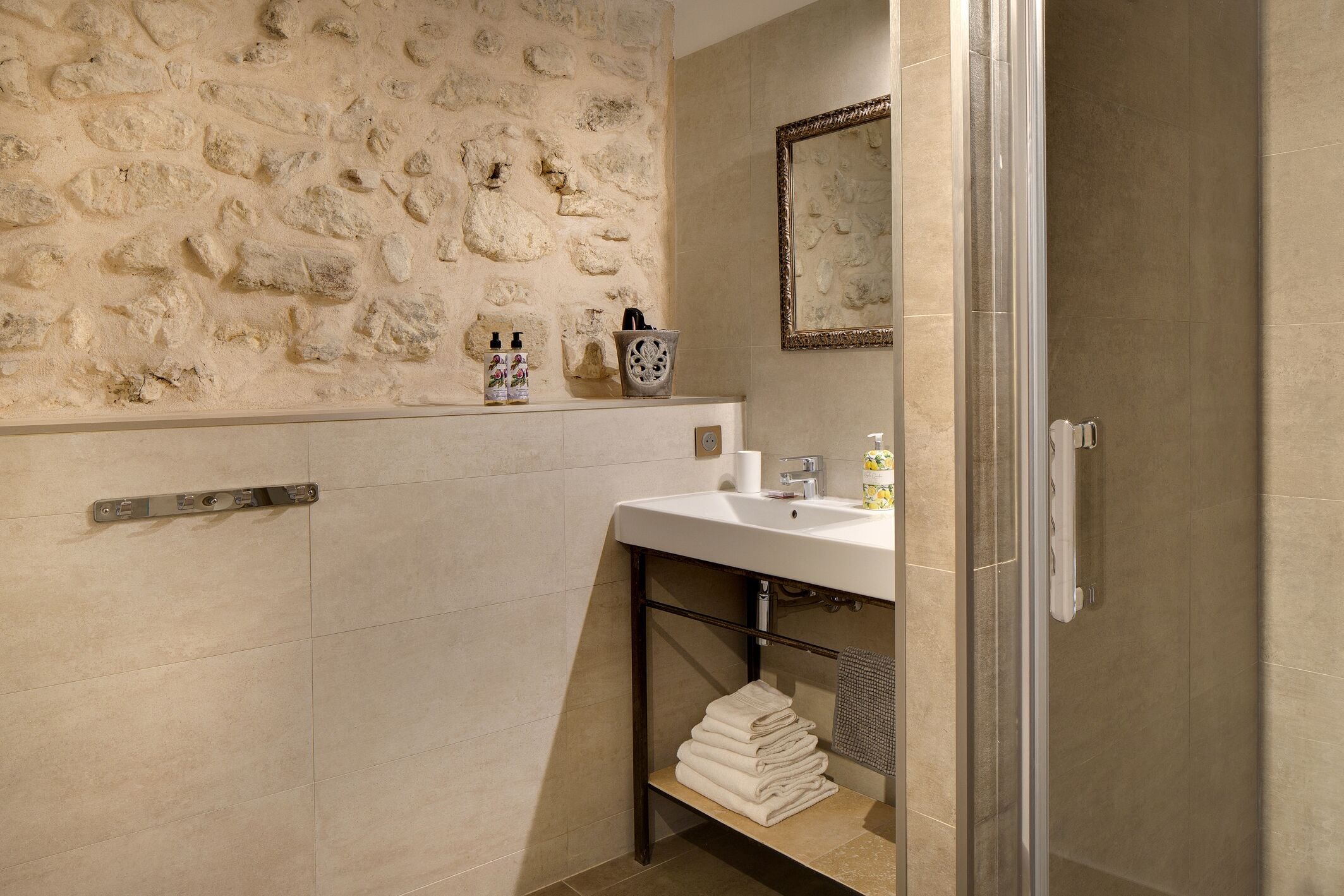A bathroom with a stone wall, a white sink, a mirror, and a towel rack.