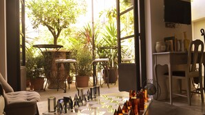 Une pièce avec une grande fenêtre, une table sur laquelle sont disposés des jeux d’échecs, des plantes en pot et un téléviseur fixé au mur.
