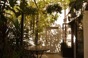 A sunlit patio with a round table, surrounded by lush greenery and hanging flower baskets. - La Maison des Augustins B&B, Spa et Fitness (Avignon)