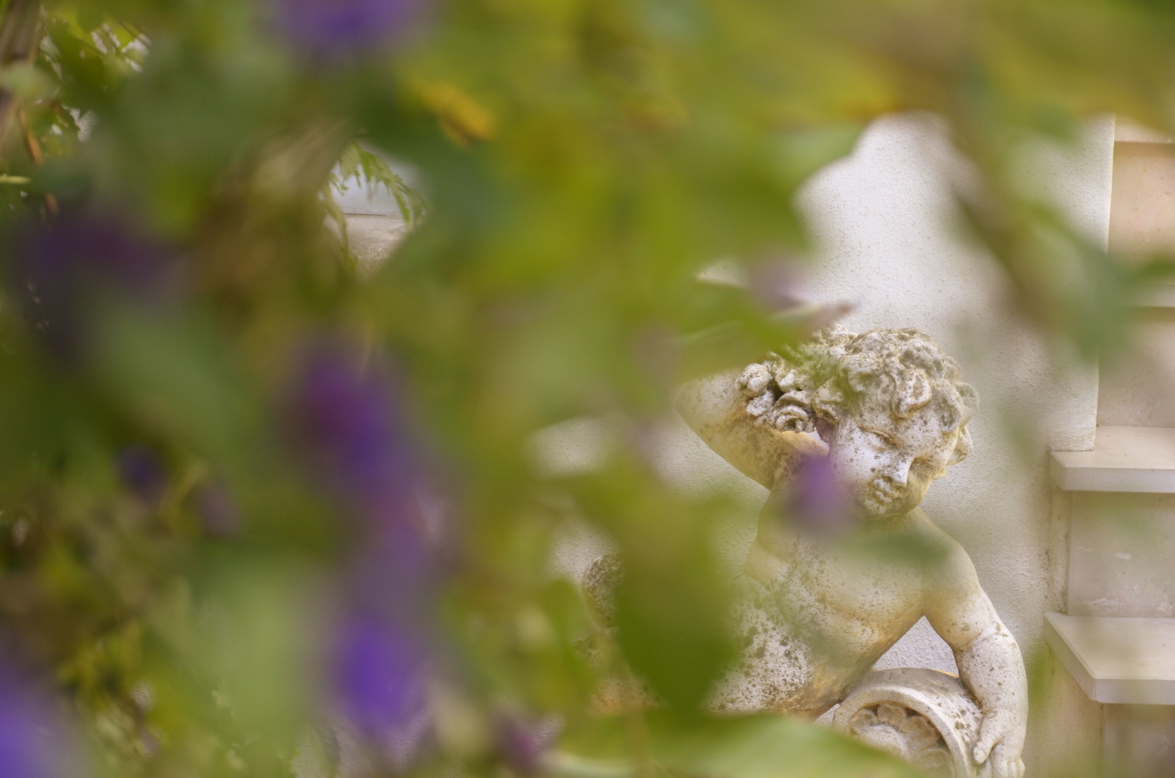 A stone statue of a child with a bucket, partially obscured by foliage.