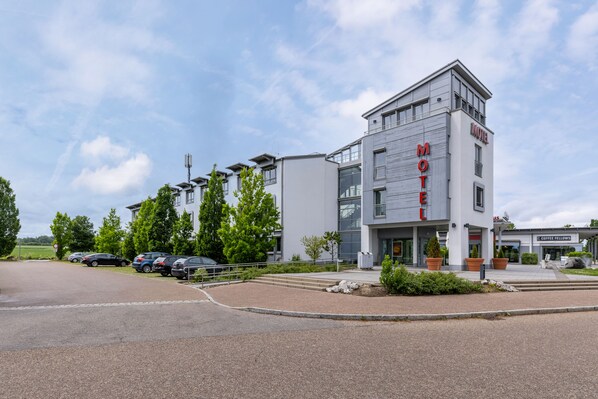 Un motel moderno con un llamativo letrero que dice 'Motel', un estacionamiento y una cafetería llamada 'Coffee Felines' al otro lado de la calle.