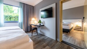 Una habitación de hotel con cama, escritorio, silla, televisor y espejo.