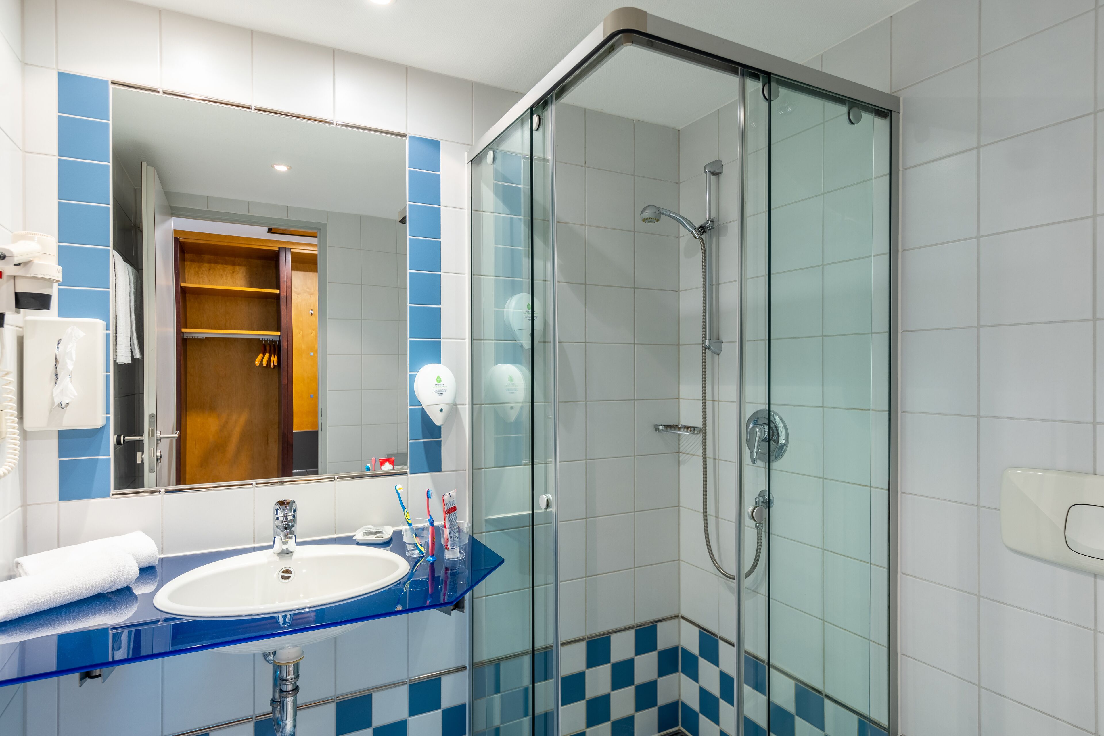 A modern bathroom with a glass shower enclosure, a blue-tiled vanity, and a large mirror.