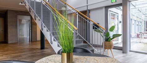 A modern indoor space with a staircase, a table with a decorative tablecloth, and potted plants.