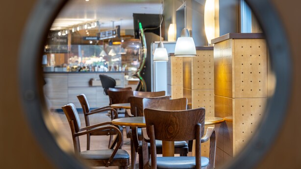 Vista circular del interior de un restaurante con mesas y sillas de madera, iluminación colgante y una zona de bar al fondo.
